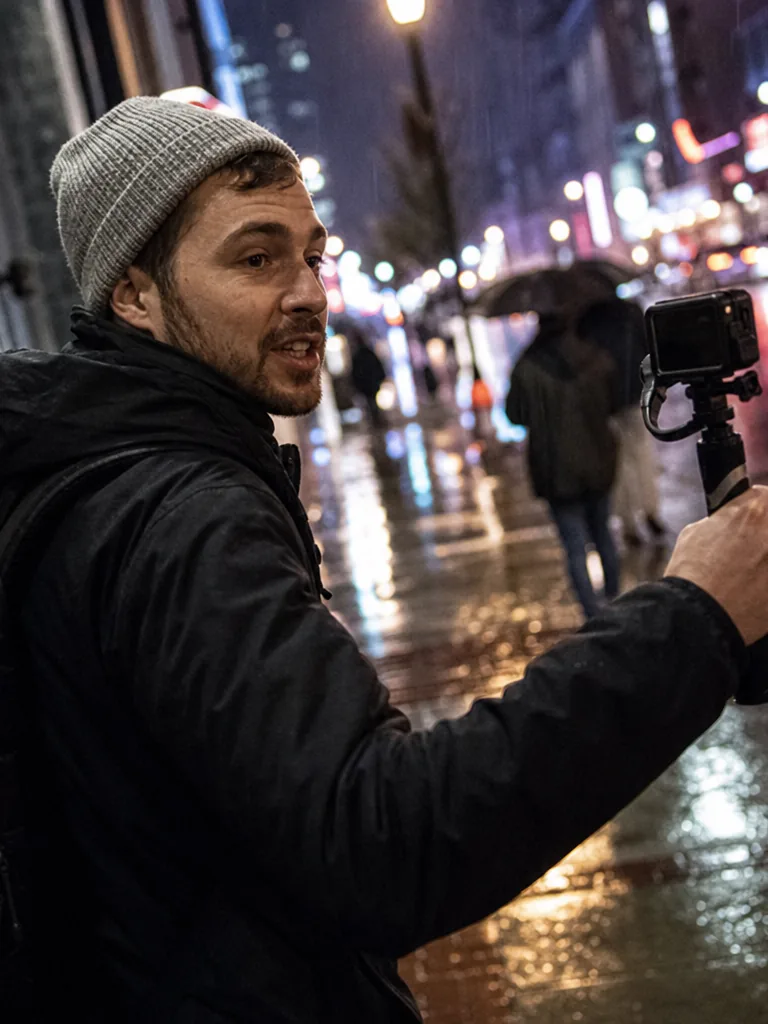 A vlogger filming himself with a handheld gimbal camera on a neon-lit city street at night