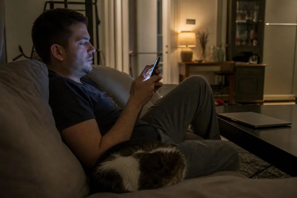 A man on a couch at night reviewing vertical clips on his phone
