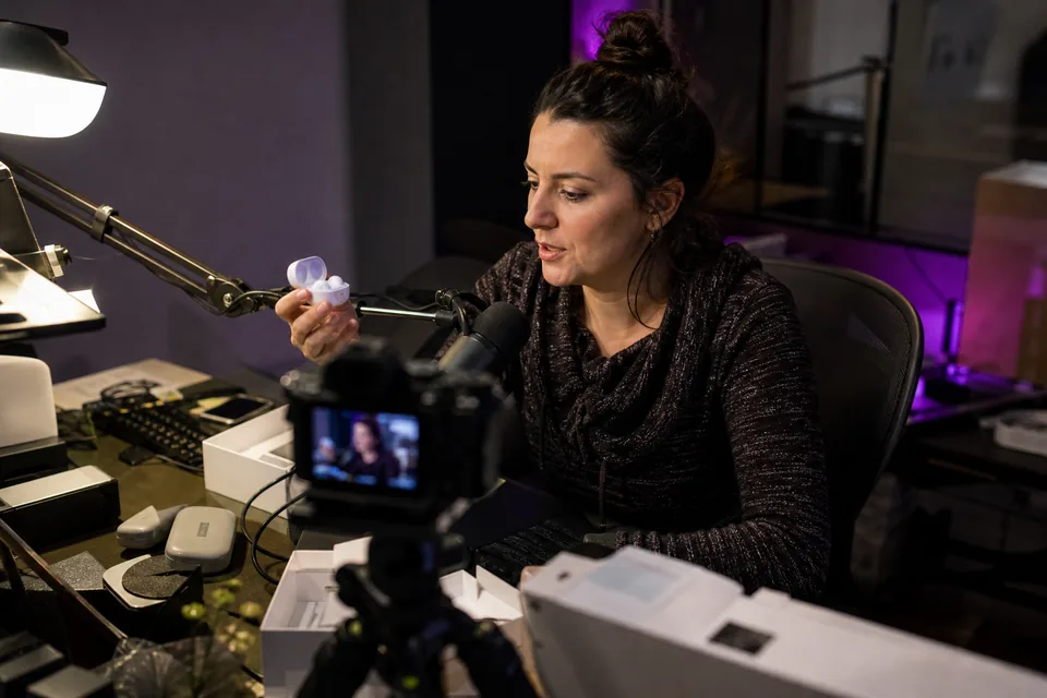 A tech reviewer talking into a boom microphone while holding a gadget up to the camera