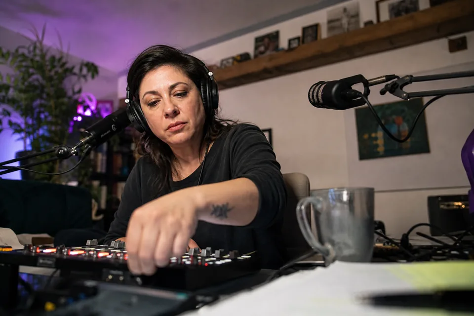 A podcast host adjusting faders on an audio mixer in a home studio
