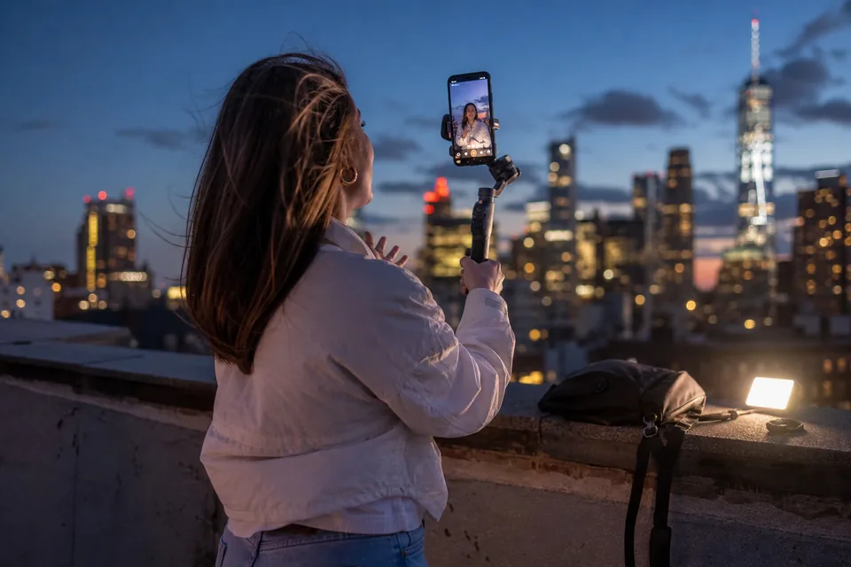 A creator filming vertical video on a phone gimbal on a rooftop at dusk
