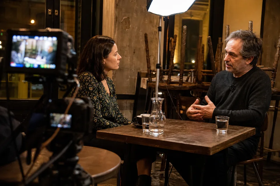 Two people recording an interview at a table in an empty cafe with two cameras on tripods